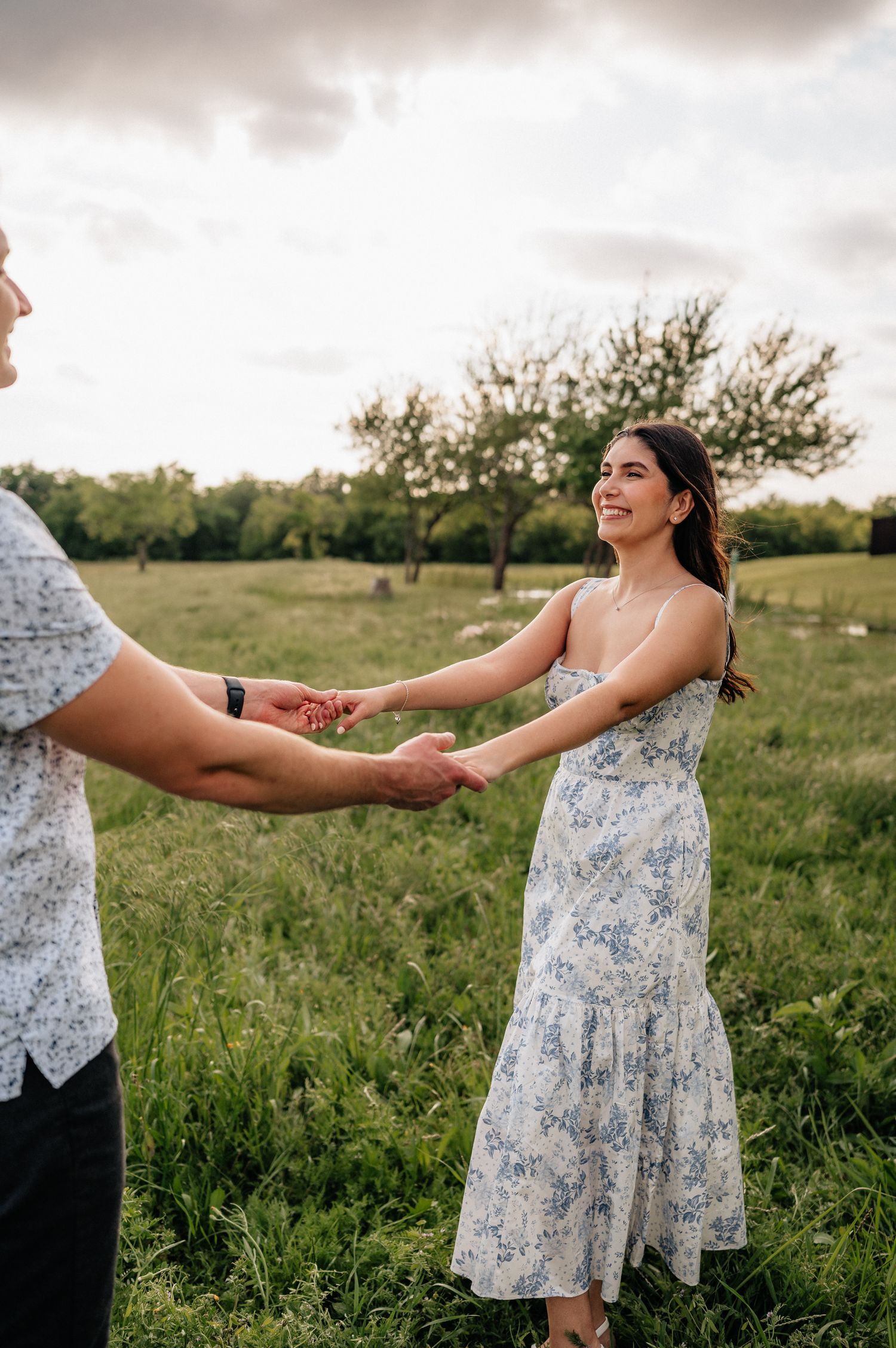 Couple holding hands and dancing in a floral dress and button-down shirt in a sunny meadow.