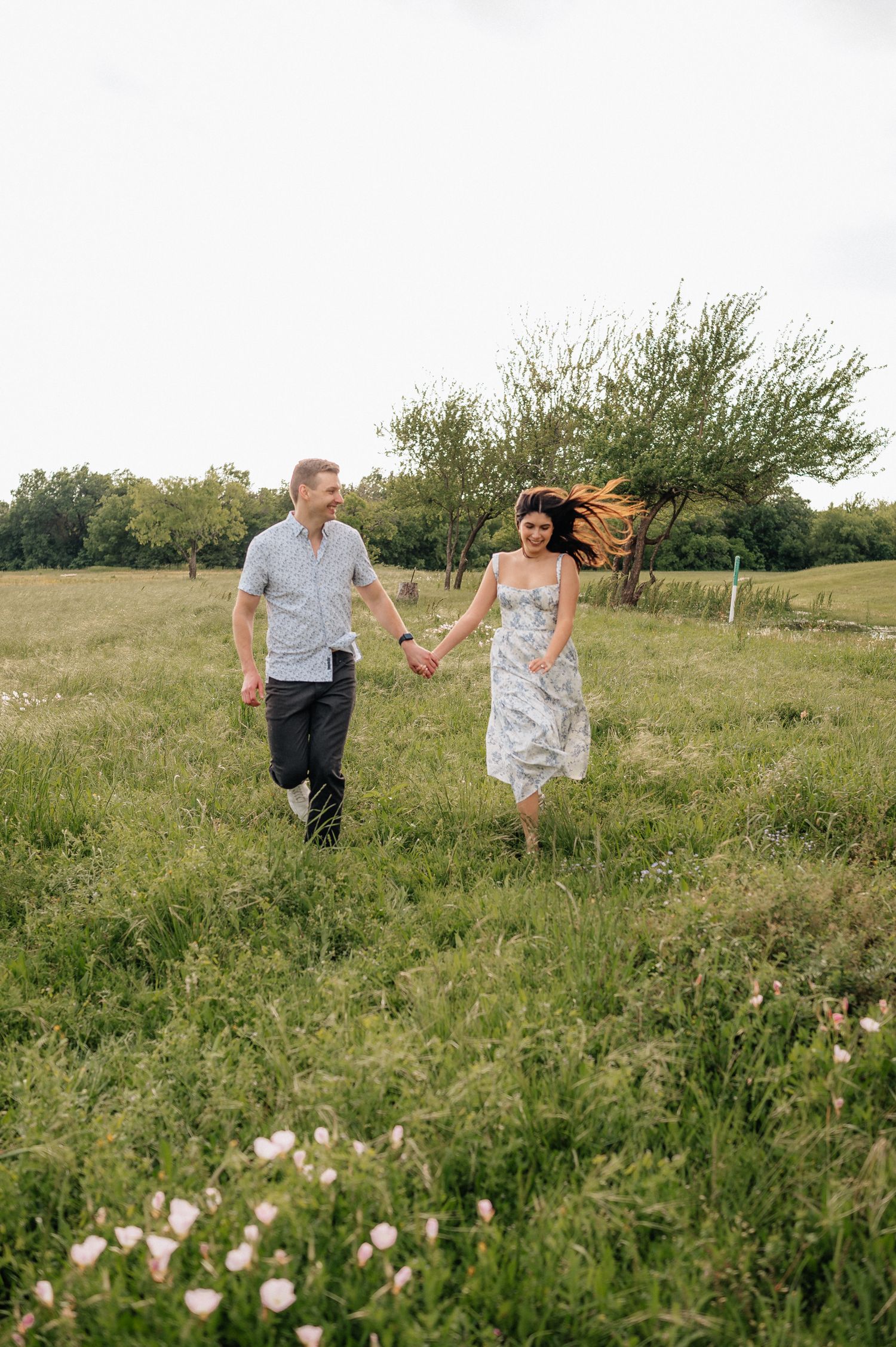 Couple holding hands while walking through a wildflower meadow on a summer evening.