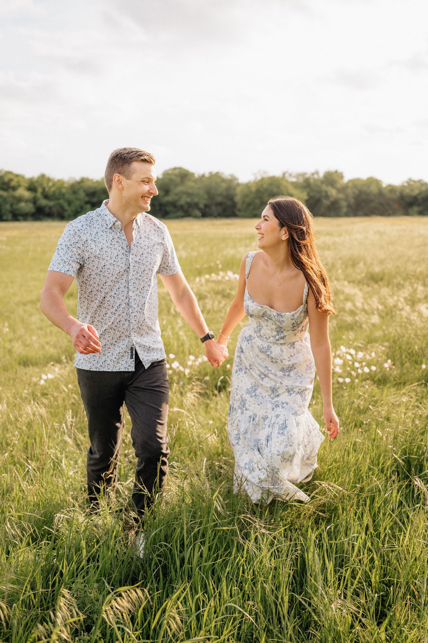 Couple strolling hand in hand through a flowering meadow in summer attire.