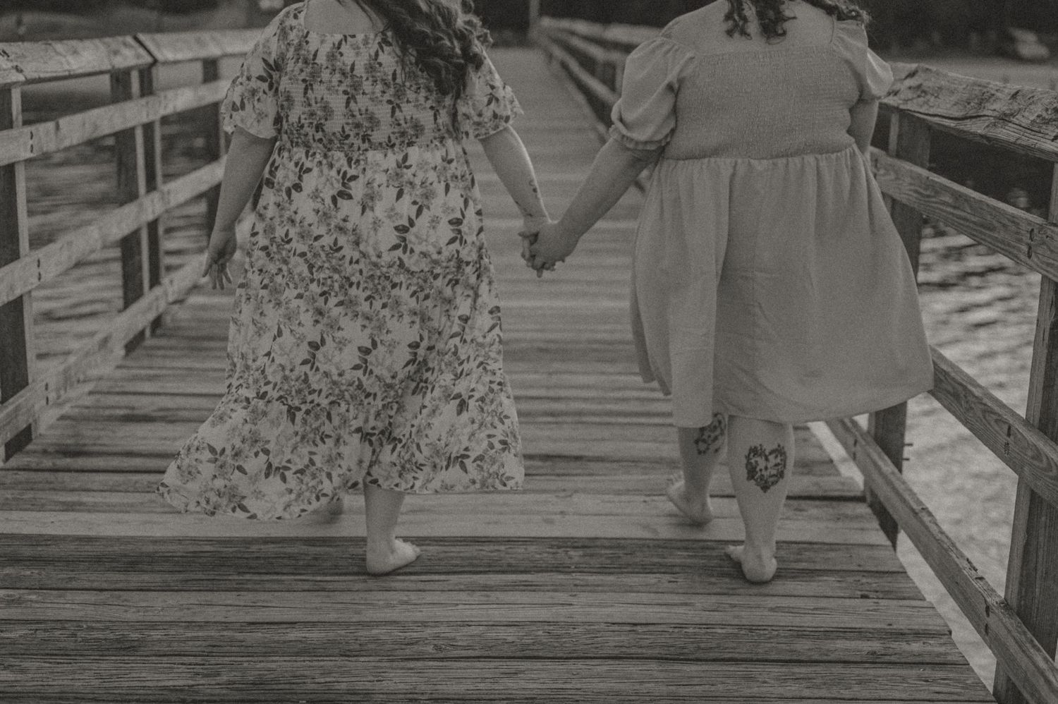 Black and white image by Samantha Campbell imagery of a lgbtq couple two walking hand in hand on a wooden boardwalk.