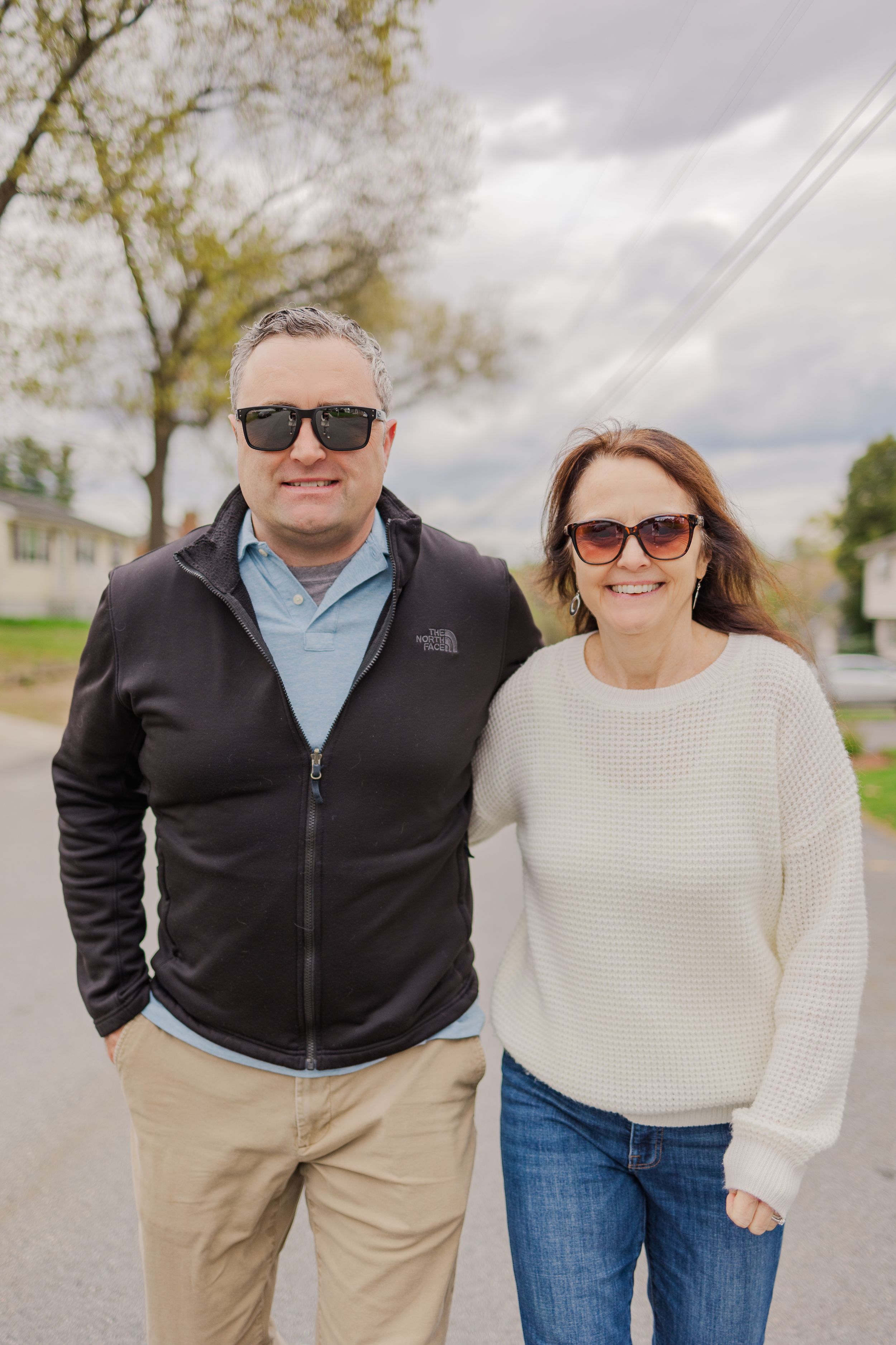 Couple in casual wear smiling on a residential street during an overcast day.