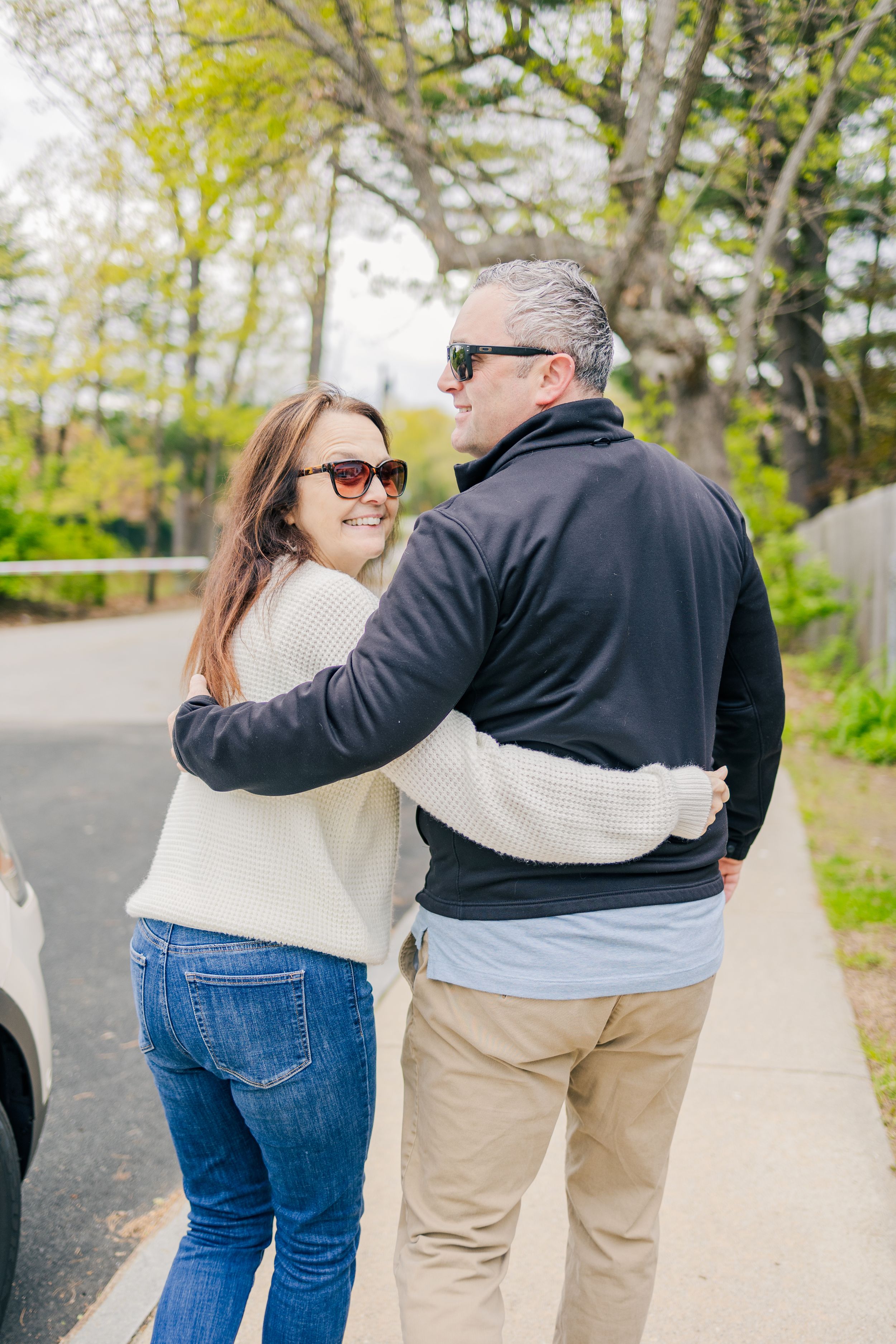 Couple walking arm in arm down a tree-lined street on a spring day.