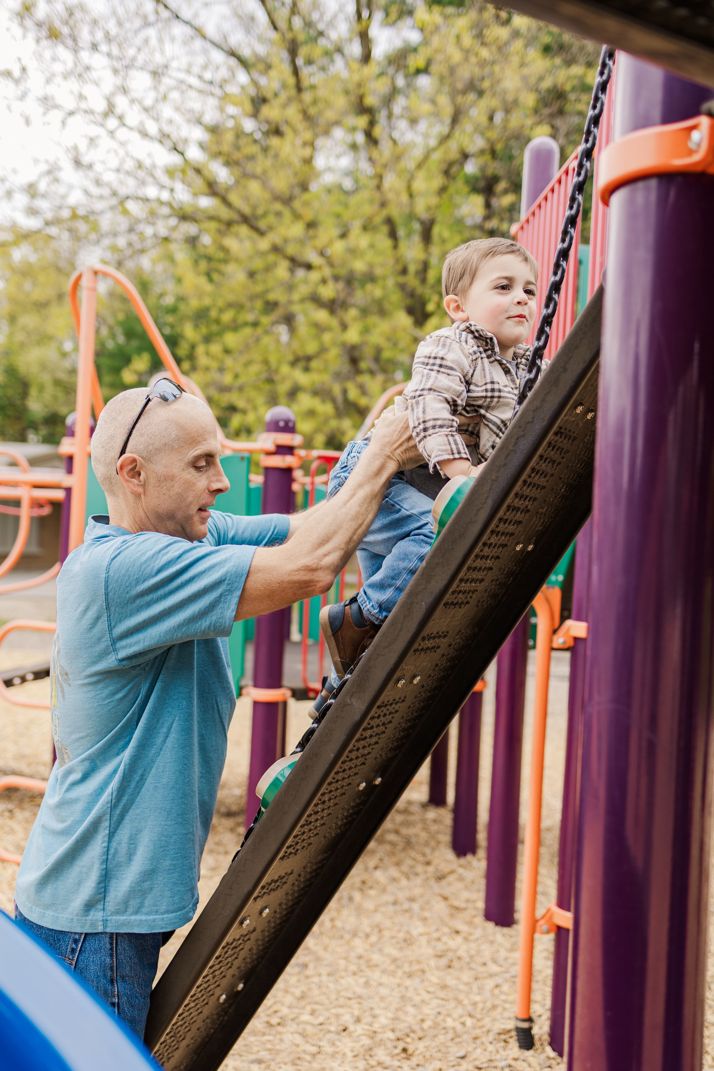 Adult helping child climb up purple and black playground structure.