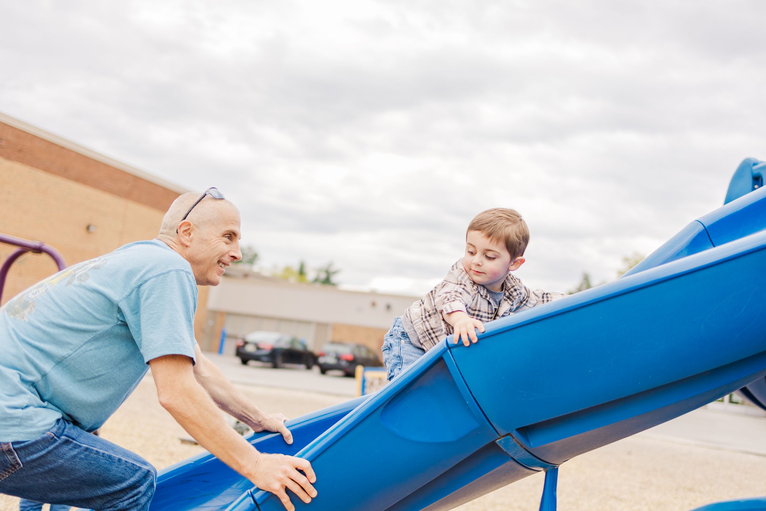 Adult and child playing on blue playground equipment under cloudy sky.