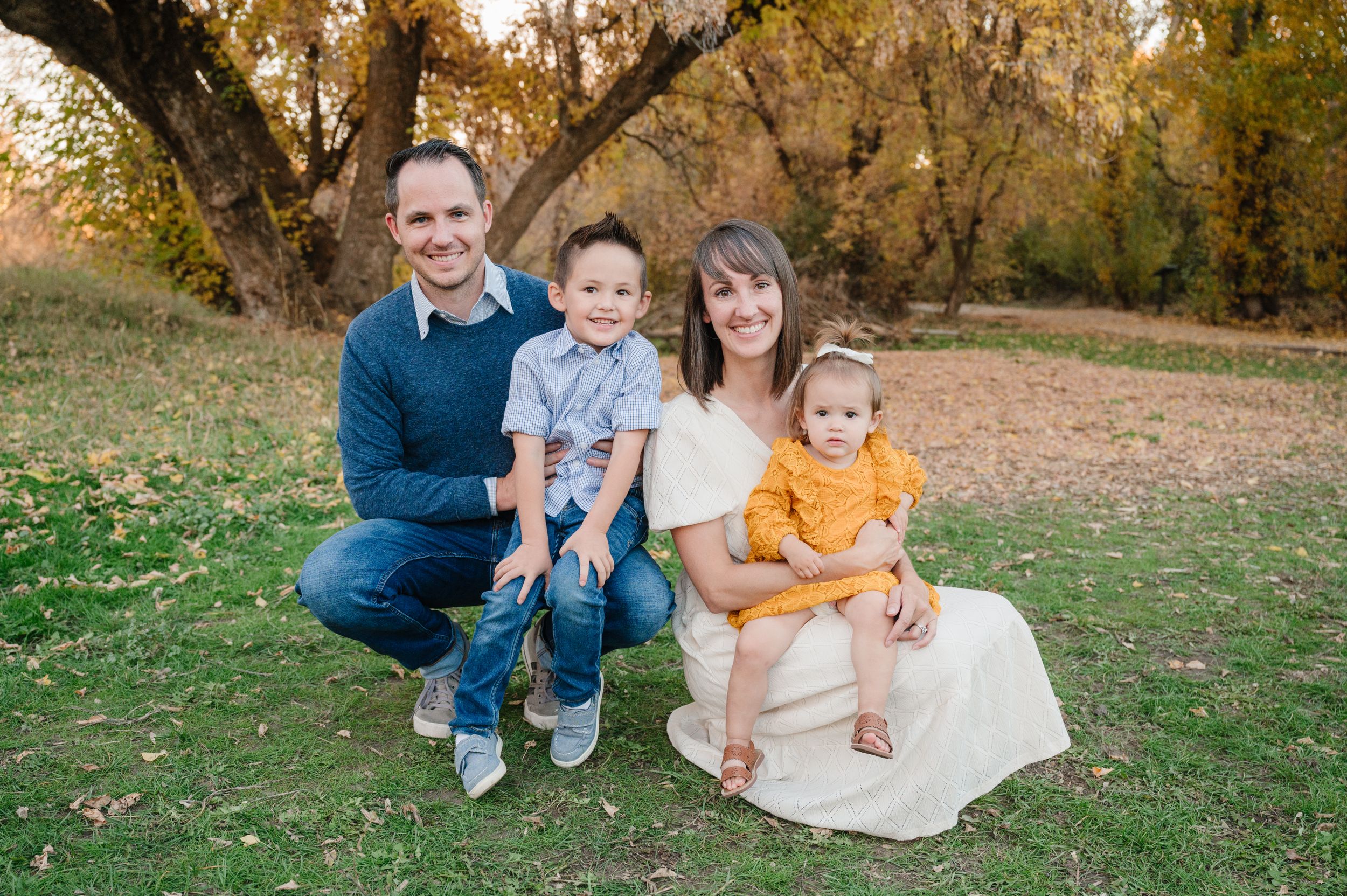 Family of four sits together on grass during golden hour autumn photo session.