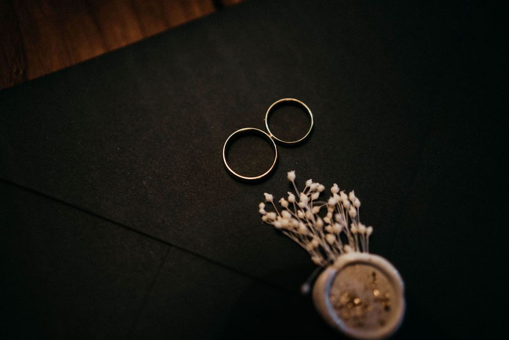 Wedding rings and delicate floral details arranged on dark background.