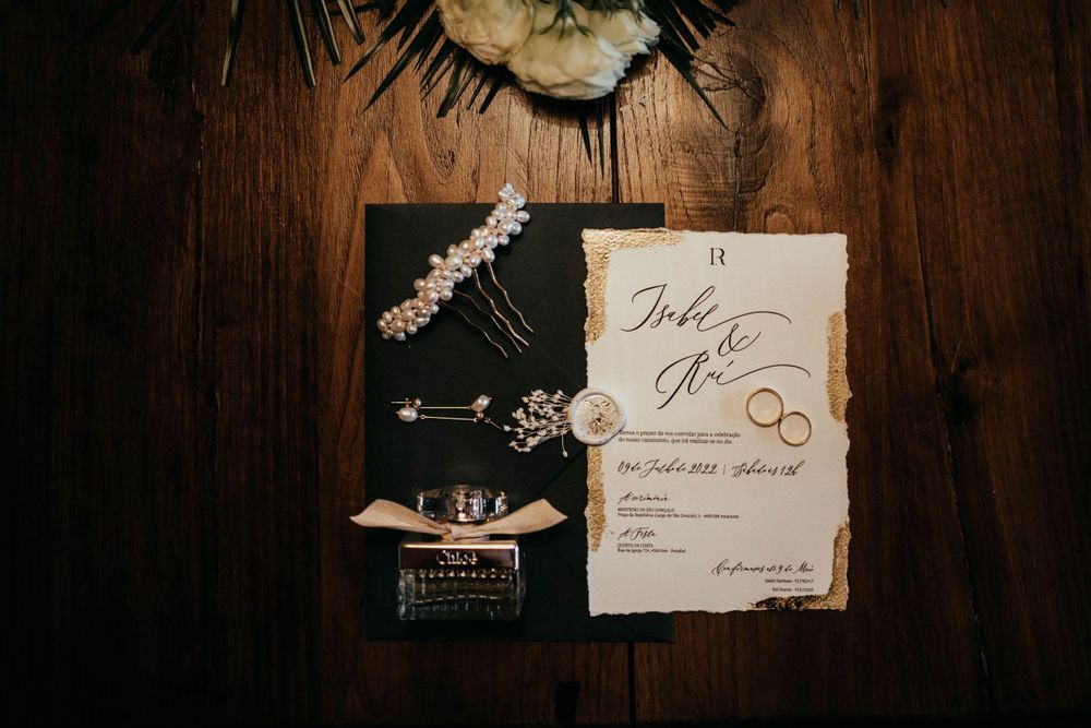 Elegant wedding invitation flatlay with rings and floral elements on dark wooden surface.