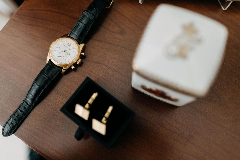 A luxury watch with black leather strap and cufflinks displayed on wooden surface.