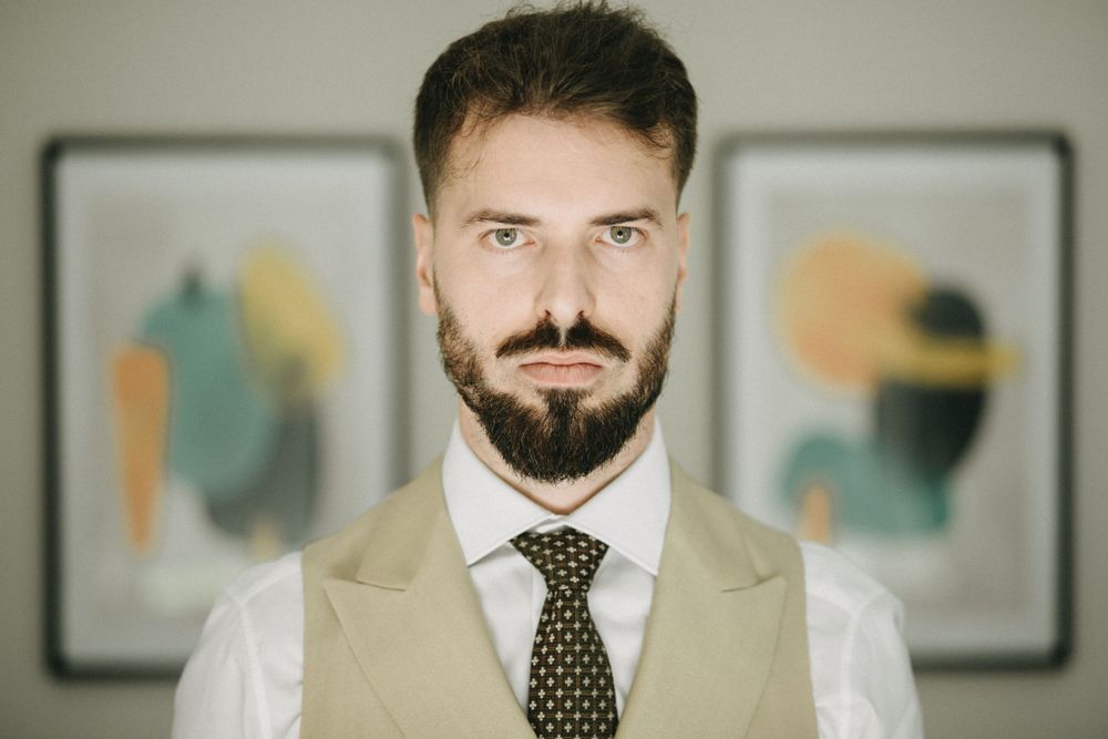 Professional portrait of person in beige suit with polka dot tie against abstract art background.