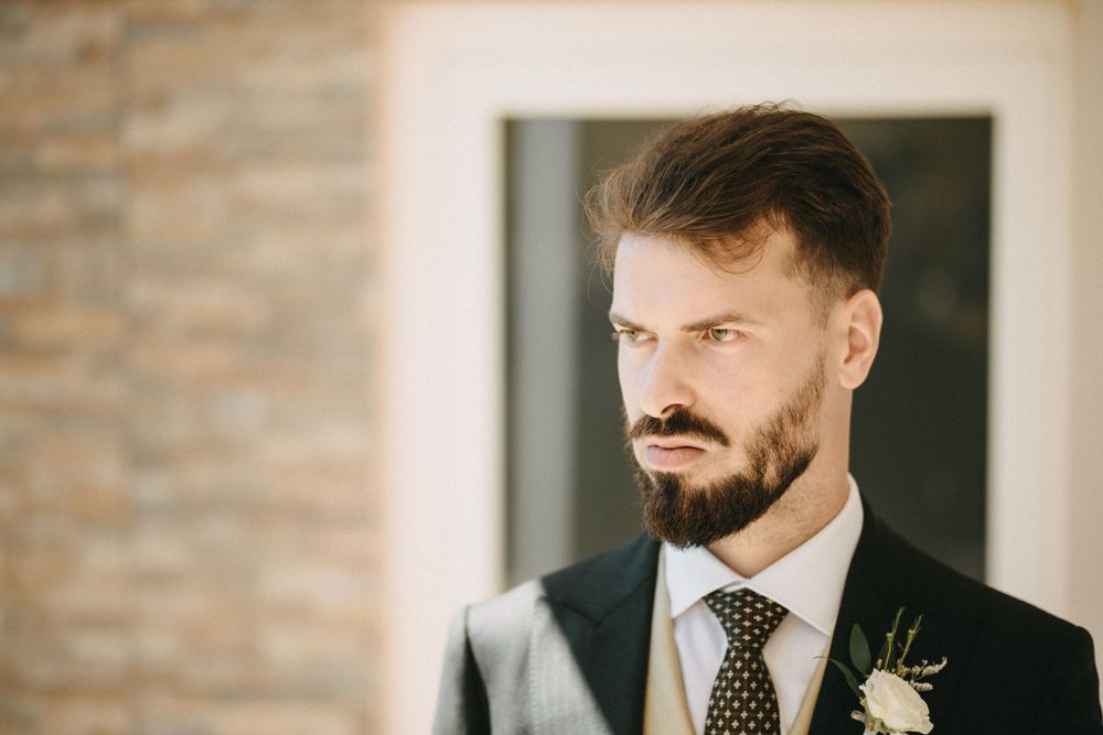Formal attire portrait with boutonniere against brick wall background.