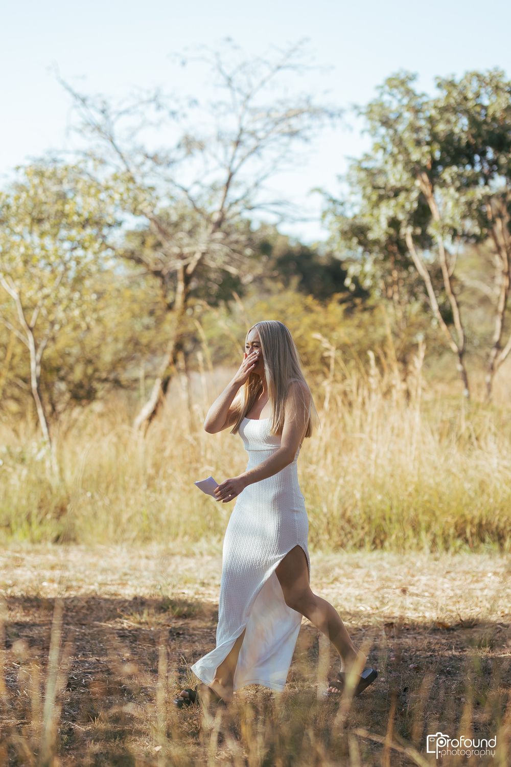 Woman in flowing white dress walking through golden grass field at sunset.
