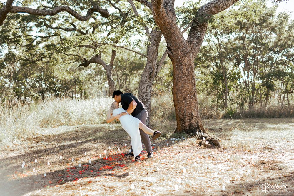 Playful couple poses under large tree branch in outdoor setting.