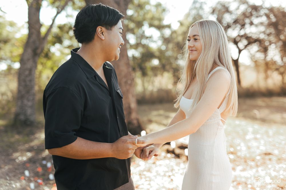 Couple shares joyful moment in white dress and black shirt against natural outdoor setting.