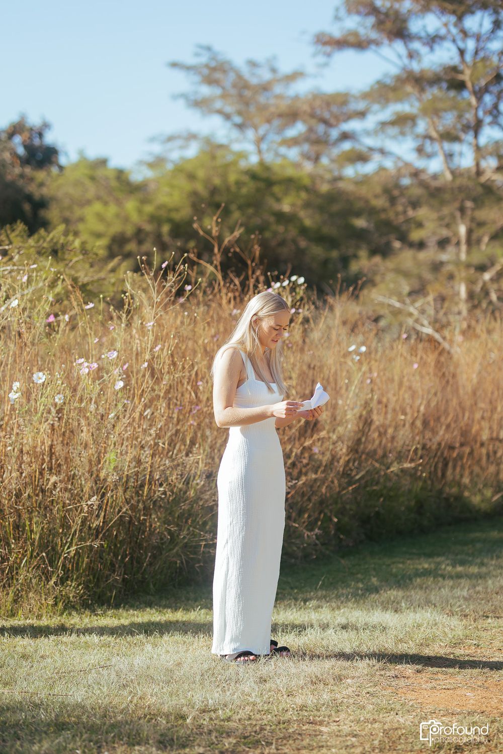 Woman in elegant white dress standing on manicured lawn reading a letter.