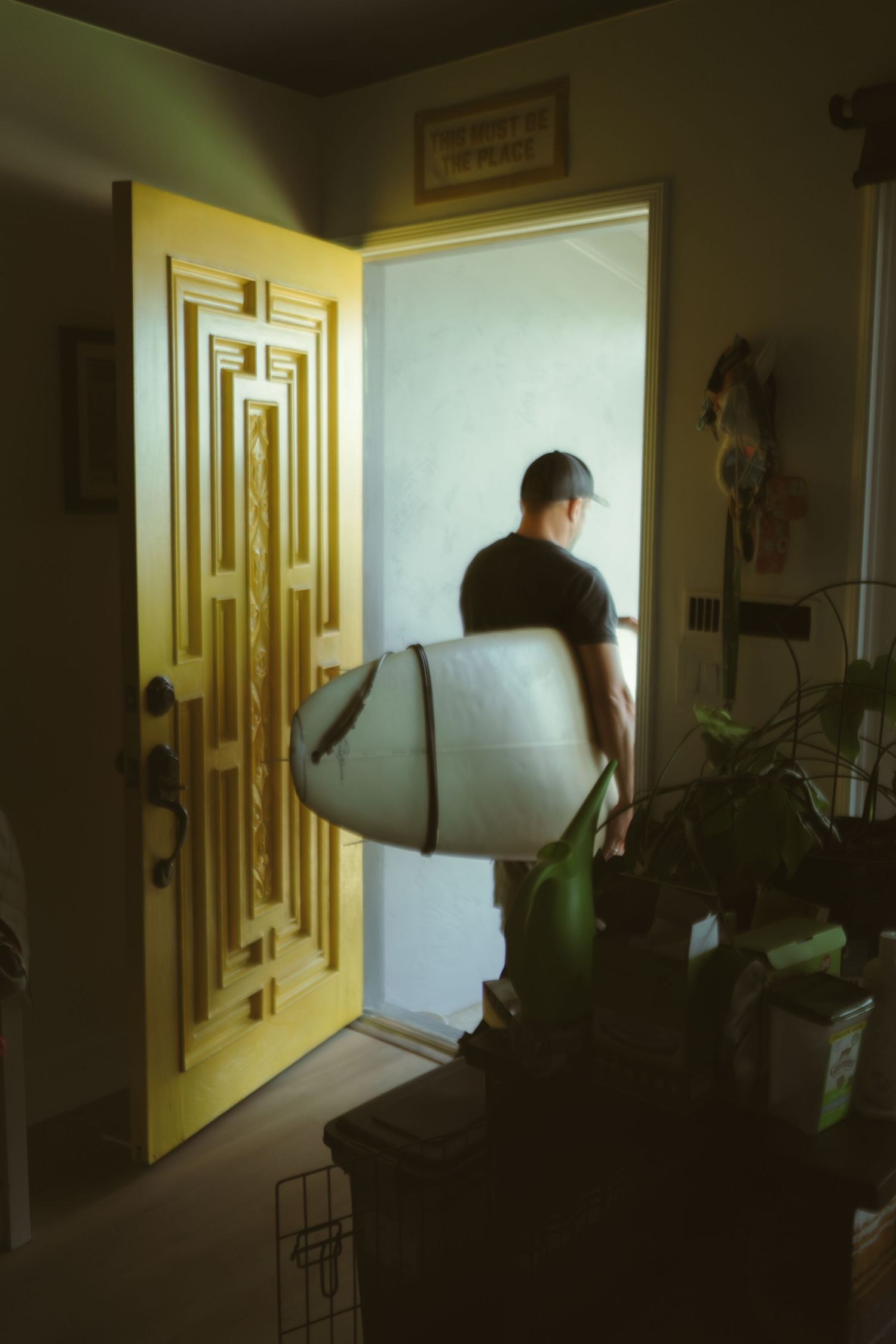 Figure carrying a surfboard through a doorway with geometric yellow door design.