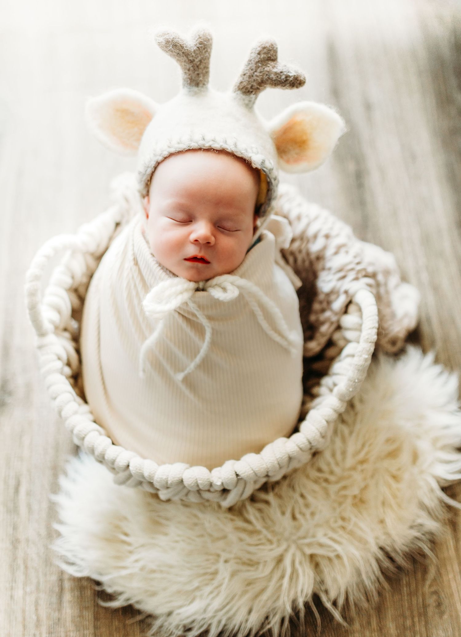 Baby wrapped in white swaddle on fluffy white blanket.
