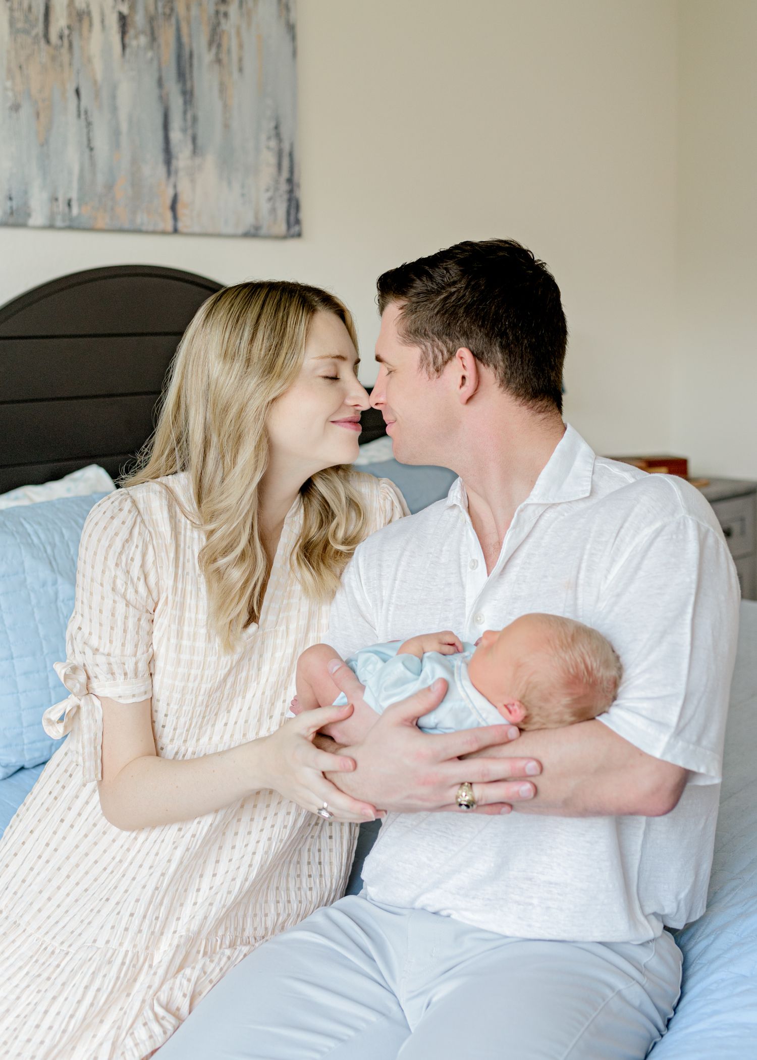 Parents share a gentle moment while holding their newborn baby in a bedroom with abstract art.