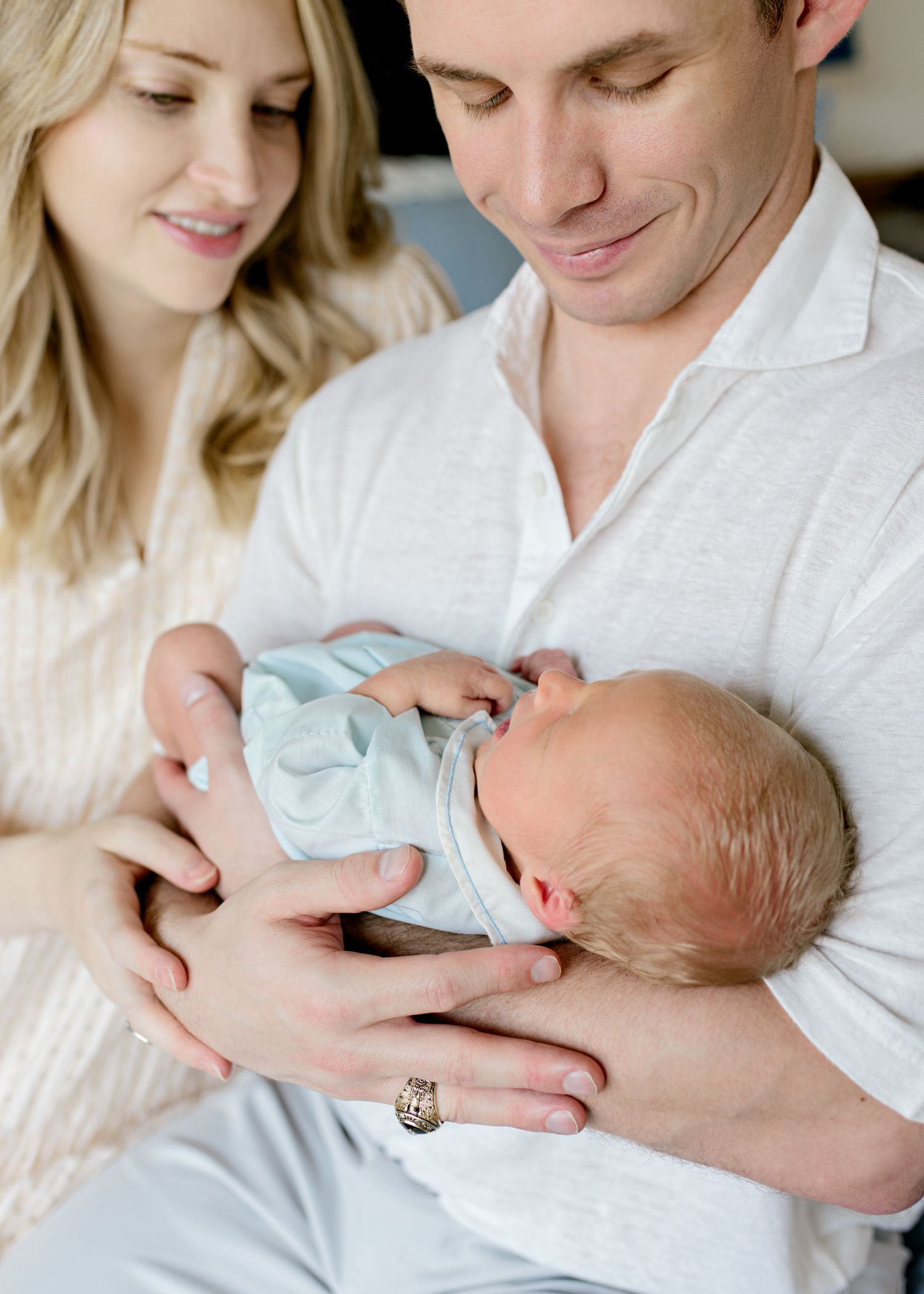 A tender moment as parents gaze lovingly at their sleeping newborn wrapped in light blue.