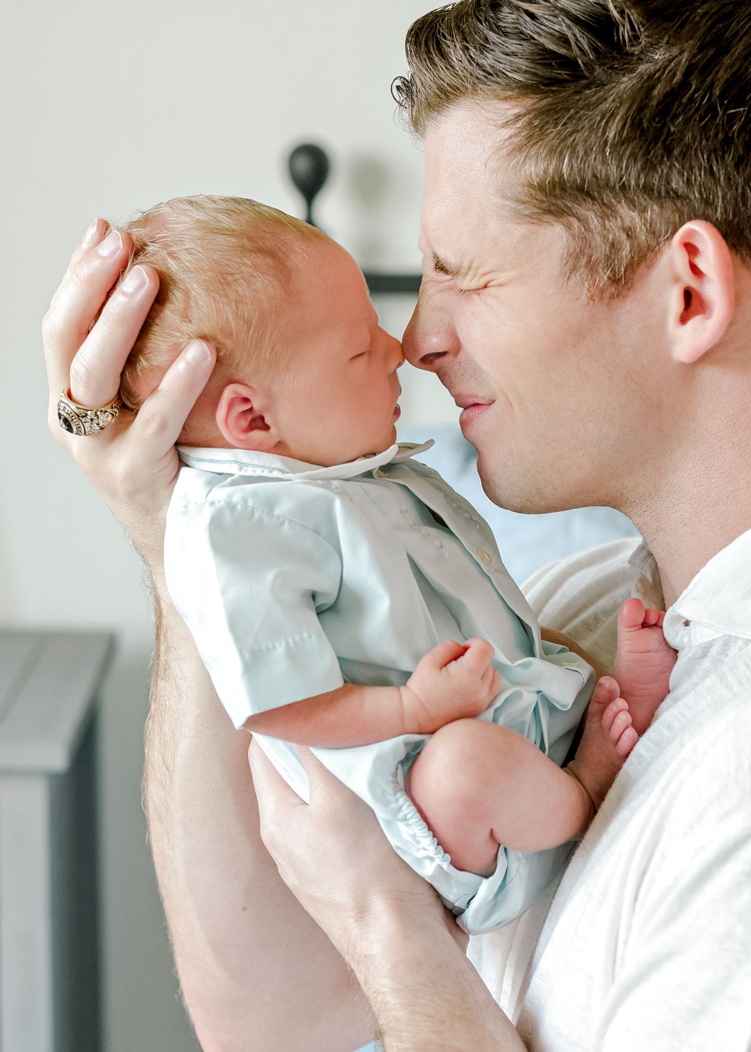 Parent in white shirt shares a close tender moment with newborn baby dressed in light blue.