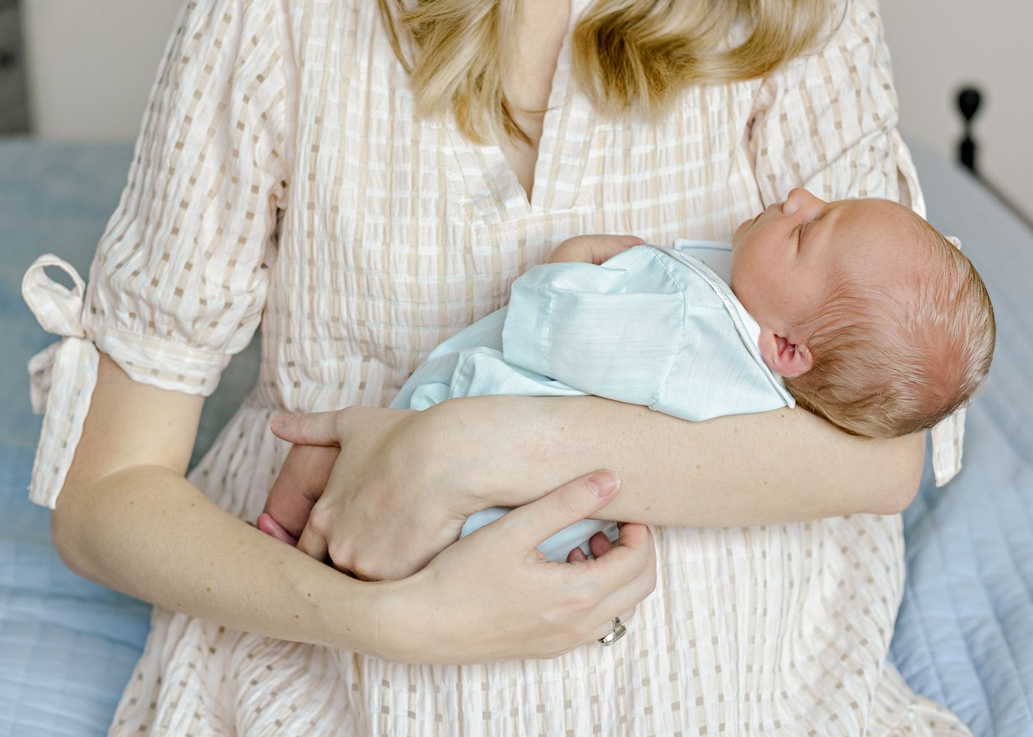 A newborn baby wearing light blue sleeps peacefully while being cradled in someone's arms.