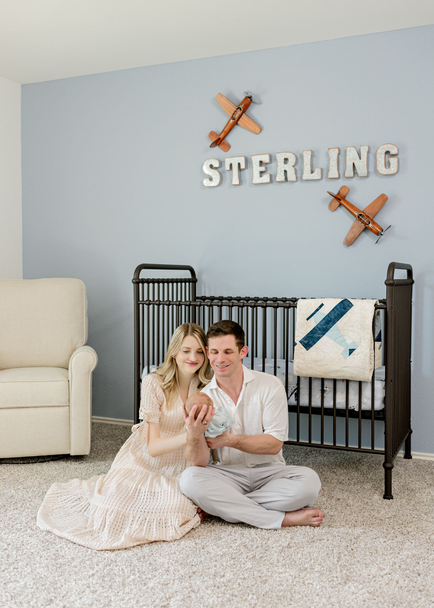 Cozy nursery scene with black crib, airplane decor, and plush beige armchair.