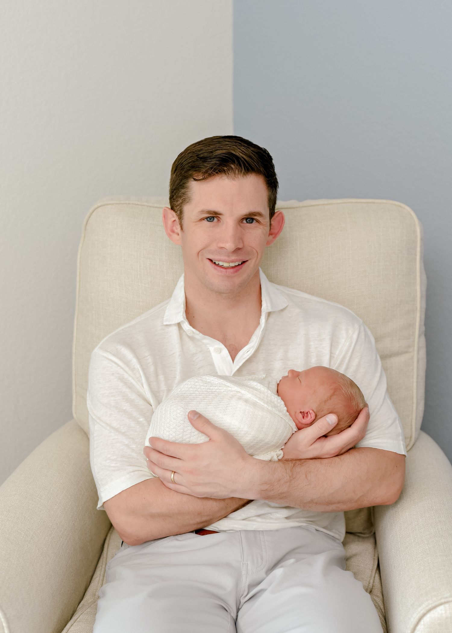 Gentle moment with newborn baby being held in cream colored armchair.