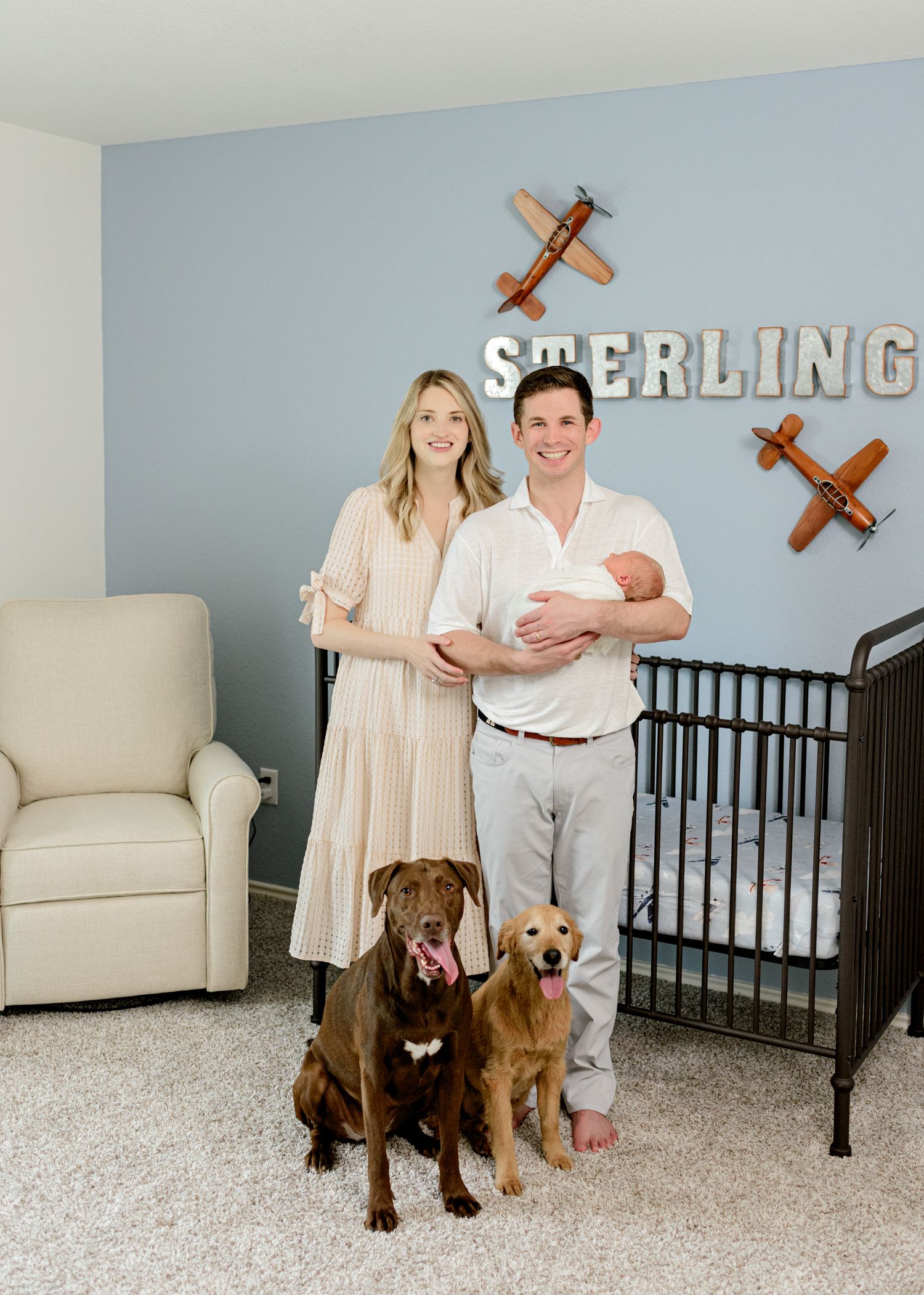 Family portrait with newborn baby and two dogs beneath wooden airplane decor.