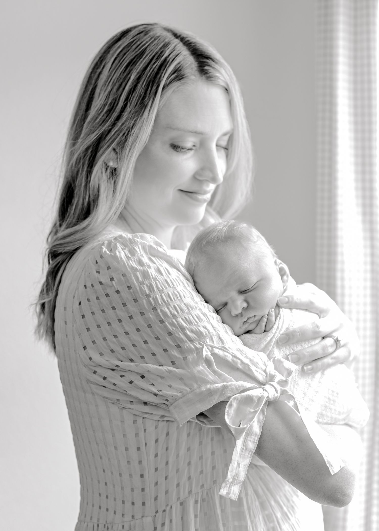 Mother embraces sleeping newborn in black and white portrait.