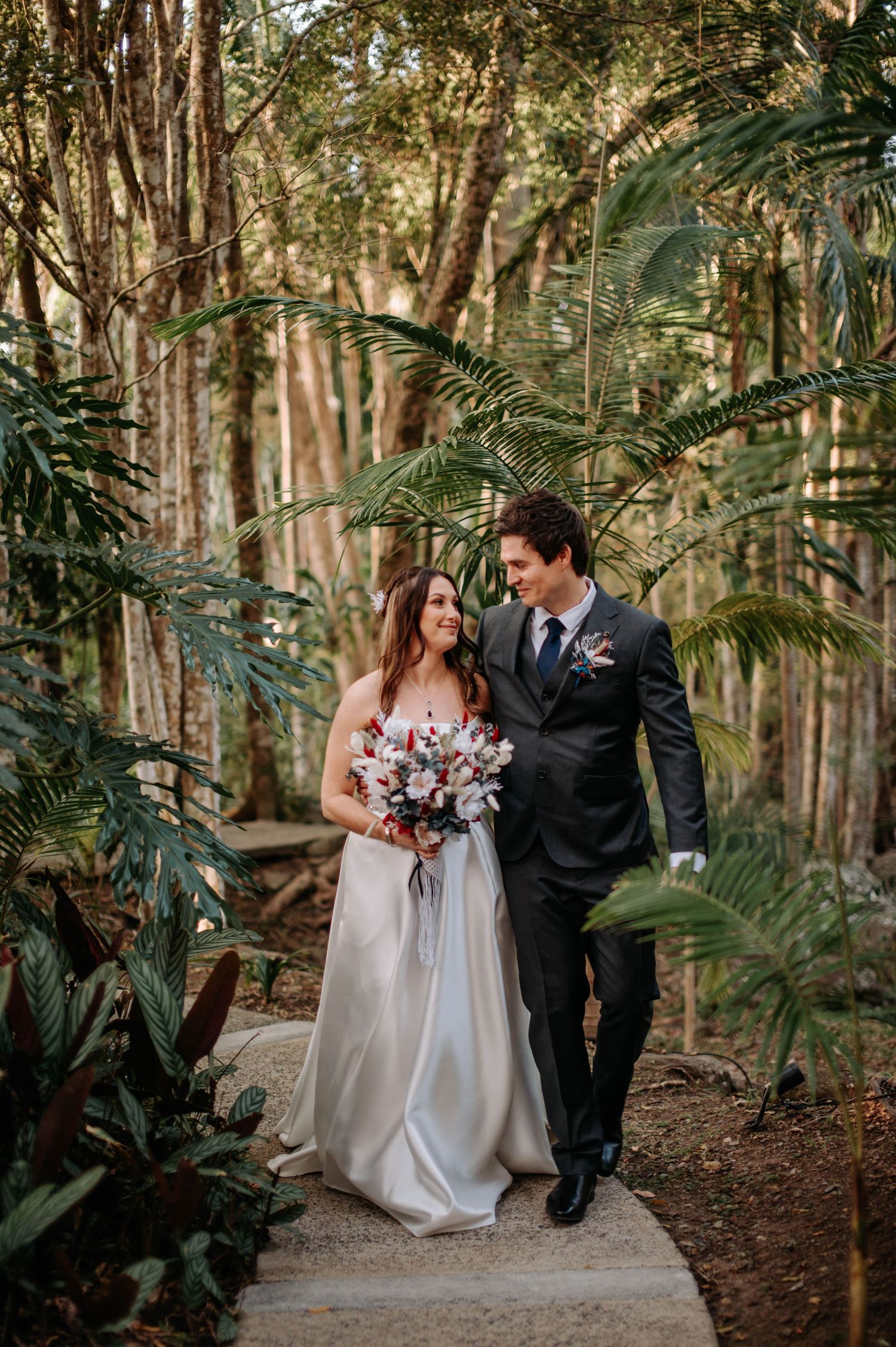 Couple walks together on garden path through lush tropical forest setting.
