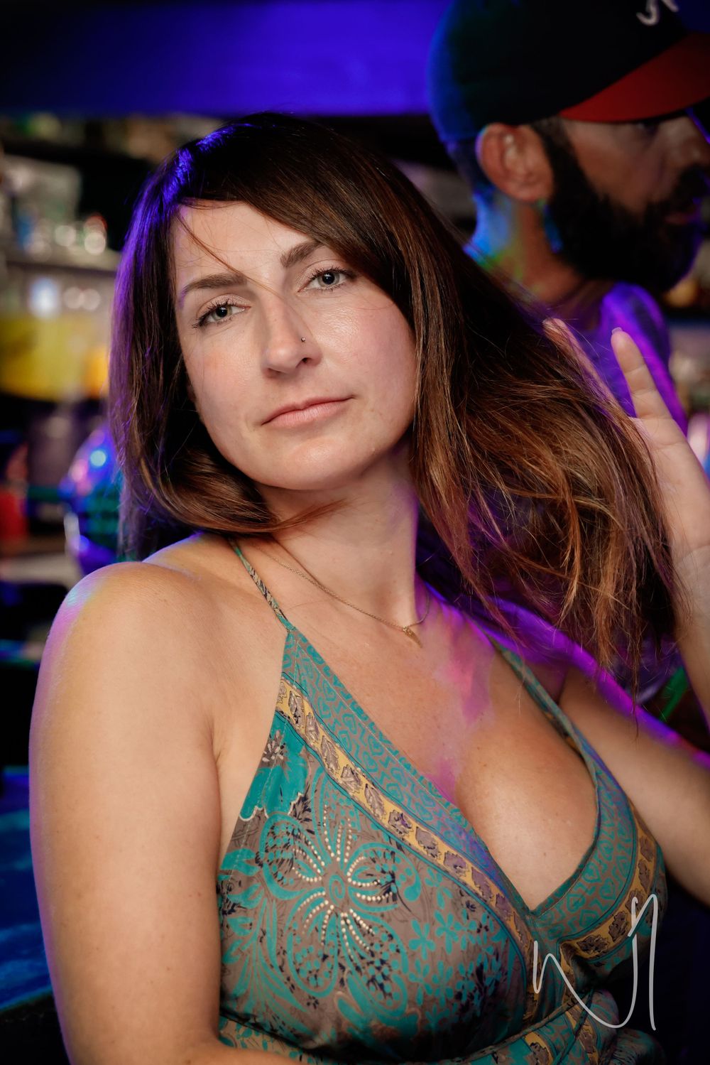 Woman in a teal lace top smiling at a nightclub with purple lighting.