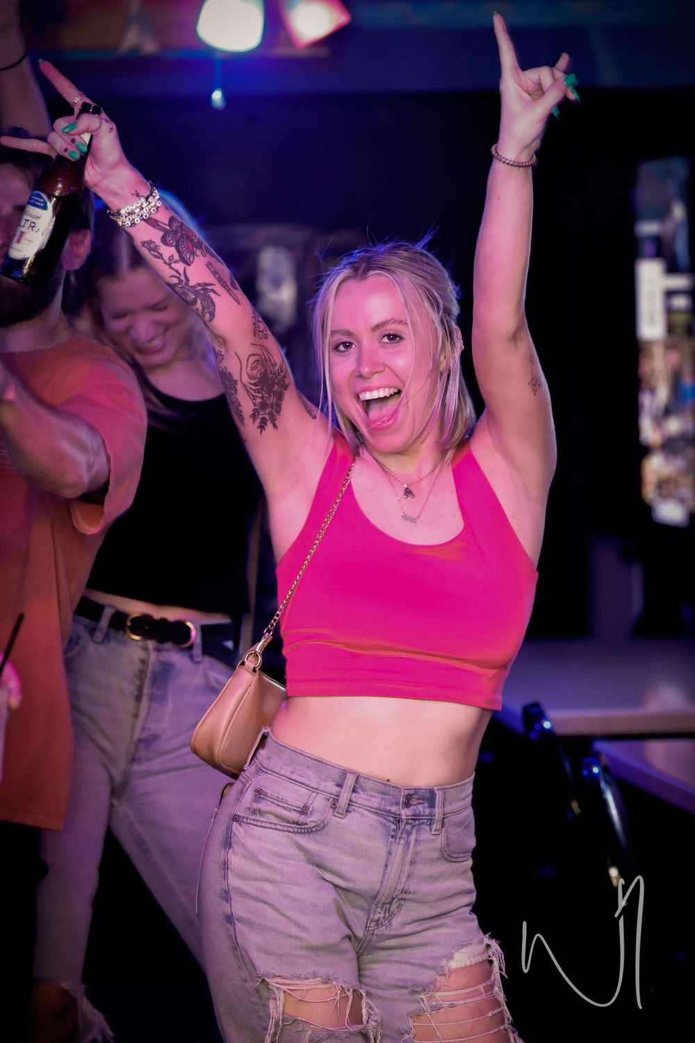 Person in pink crop top and denim shorts dancing energetically at a nightclub.
