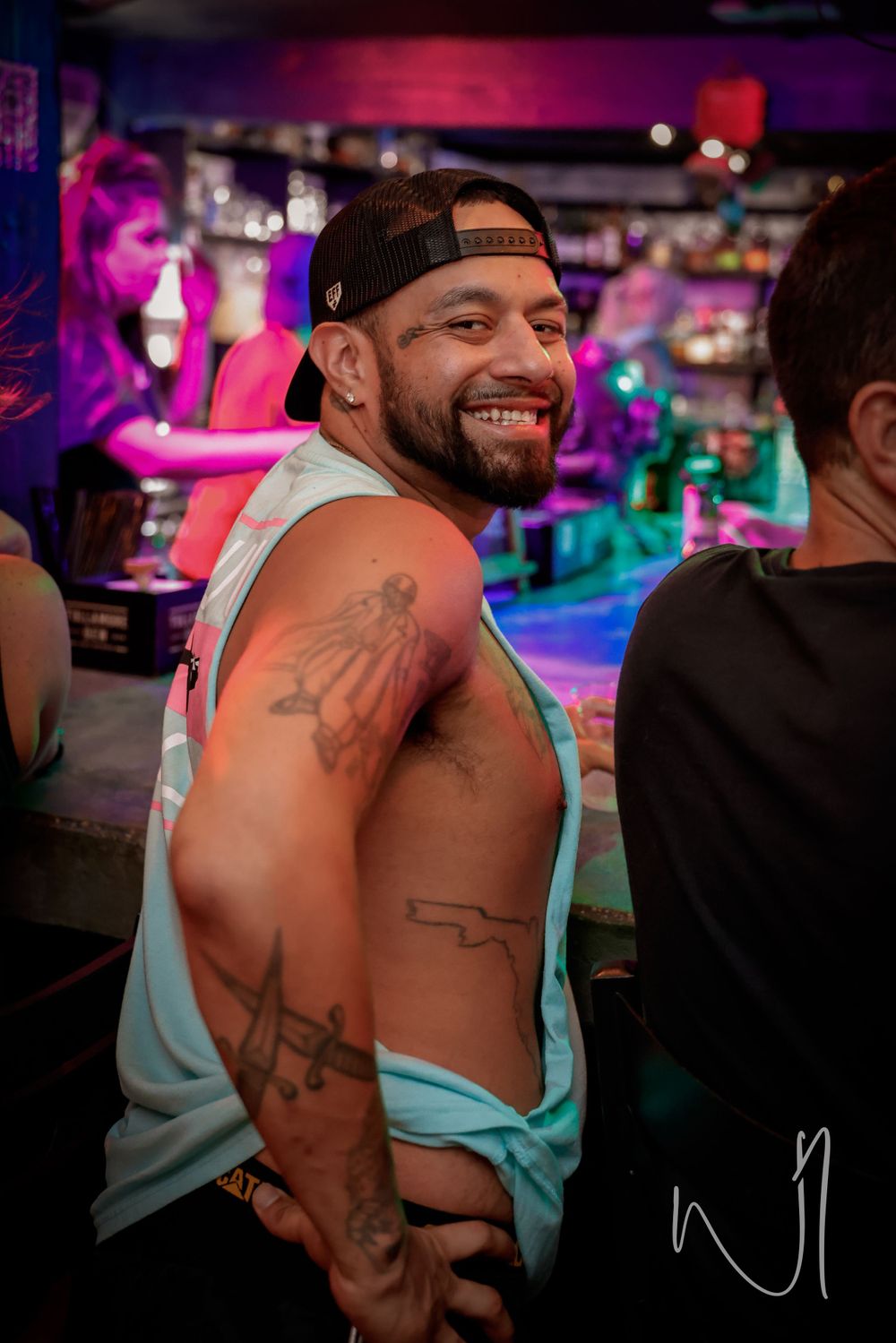A person showing off colorful tattoos on their back in a club setting with neon lighting effects.
