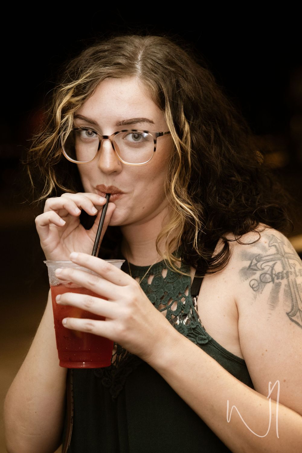 Person wearing glasses drinking from a straw in dark lighting.