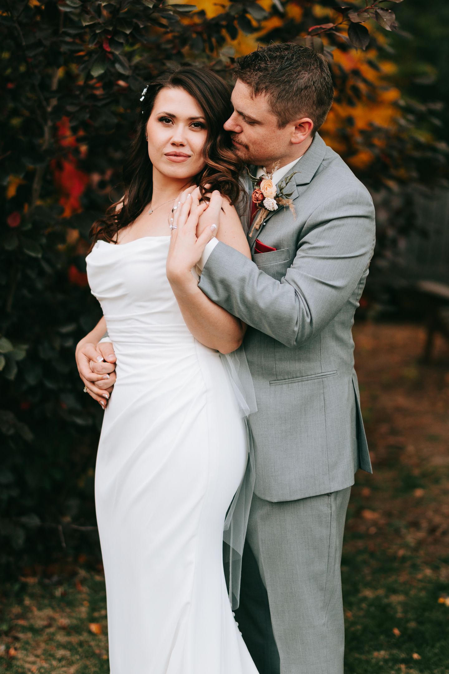 Intimate wedding portrait with couple embracing against autumn backdrop.