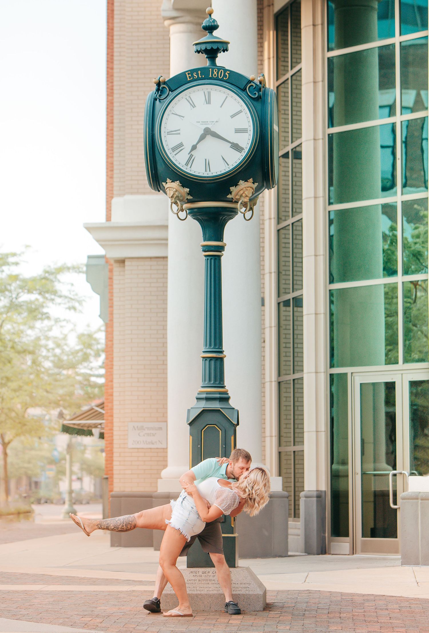 A romantic dip pose in front of a decorative clock tower on a brick sidewalk.