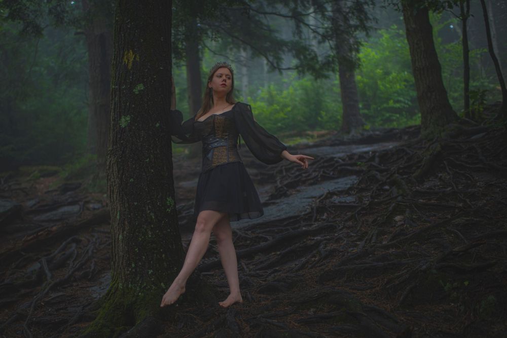 Ethereal forest scene with dancer in black dress posed gracefully among tree roots.