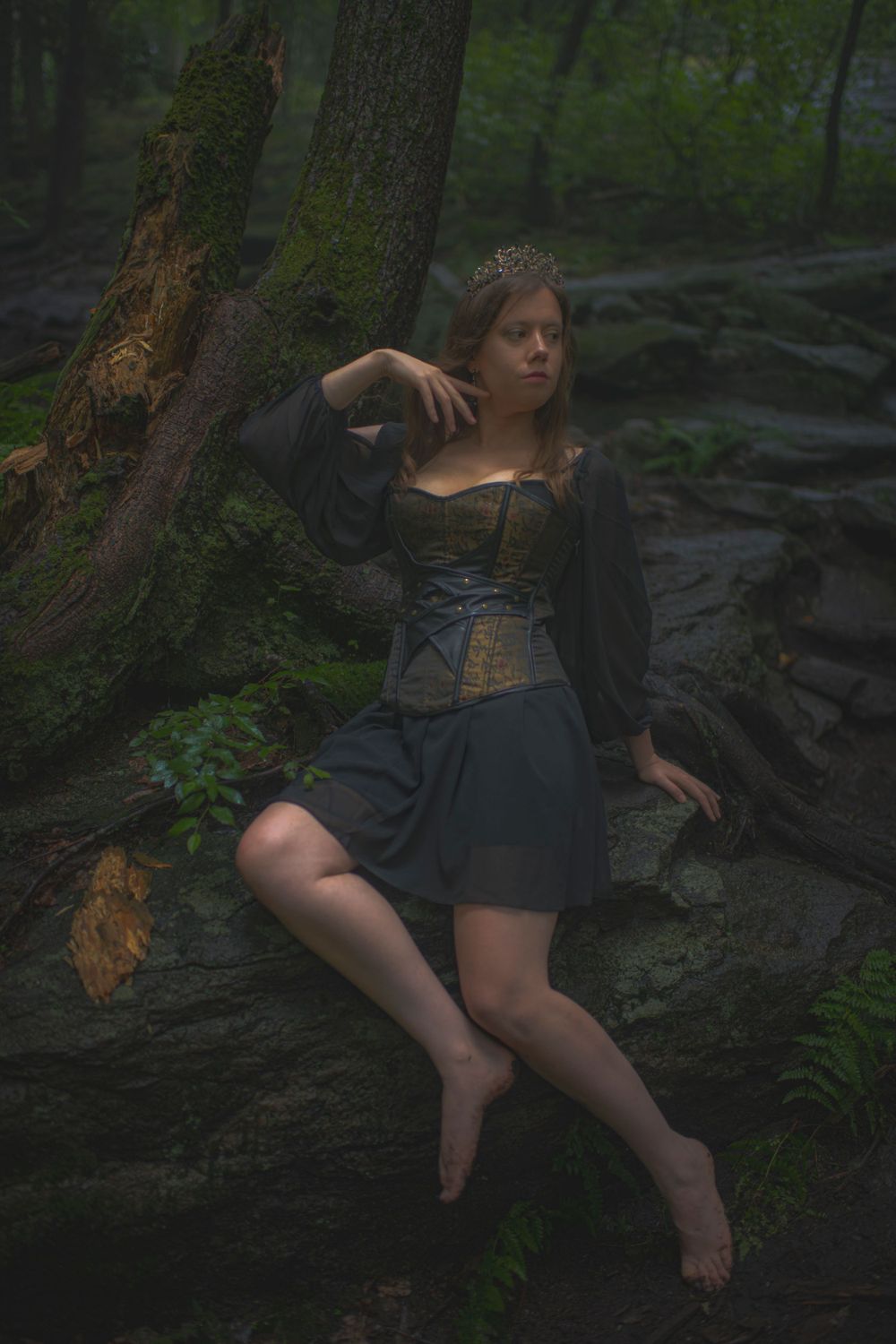 Dramatic pose against forest tree wearing vintage-style dark dress and corset.
