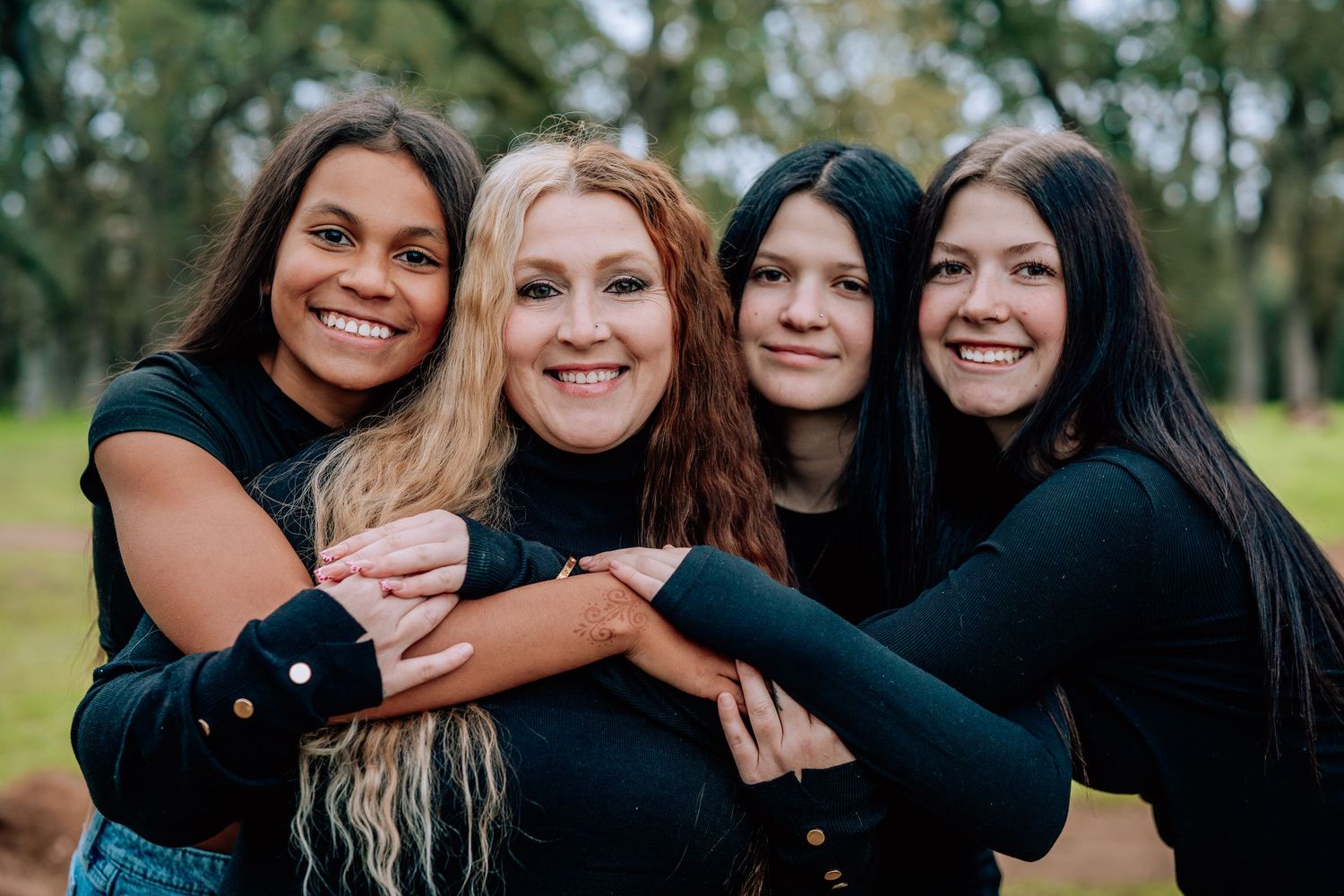 A group of friends in black outfits share warm embraces and joyful smiles during an outdoor photo session.