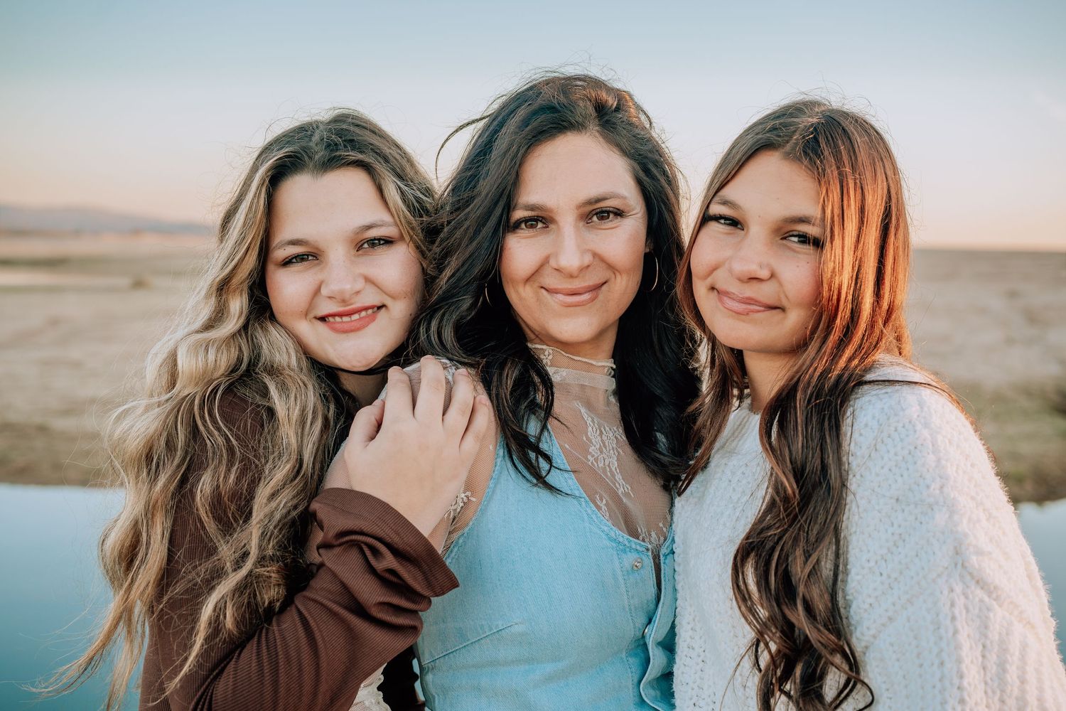 Three friends in turquoise and neutral colors pose together in a series of candid outdoor photos at sunset.