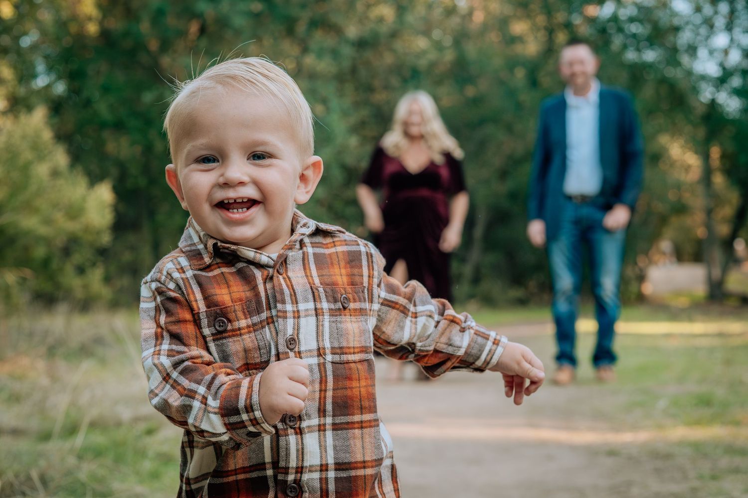 A toddler in a plaid shirt plays and laughs while enjoying a sunny autumn day outdoors in a park setting.