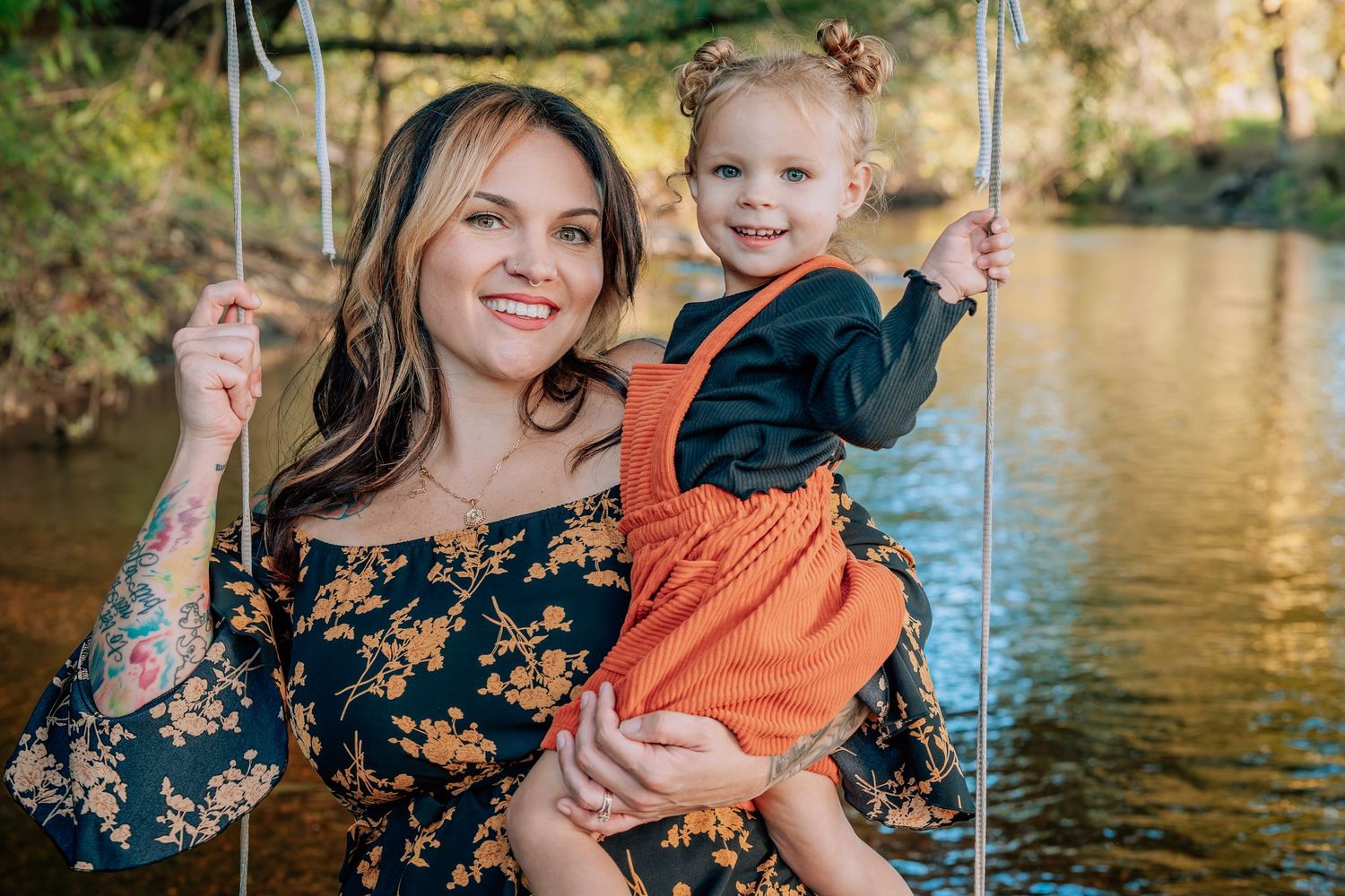 A family in floral and orange outfits poses together by a sunlit lake during an autumn photo session.