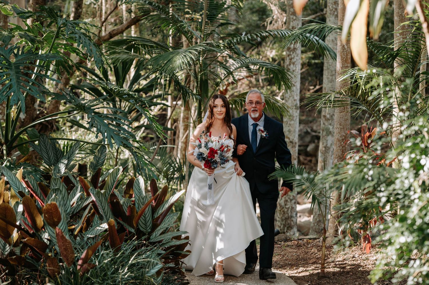 Couple walking through a lush tropical garden pathway during wedding ceremony.