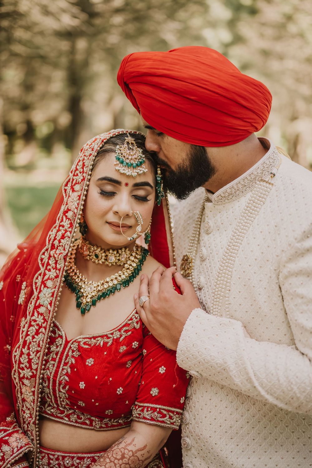 Traditional Indian wedding couple in red and cream attire posing for romantic portraits.