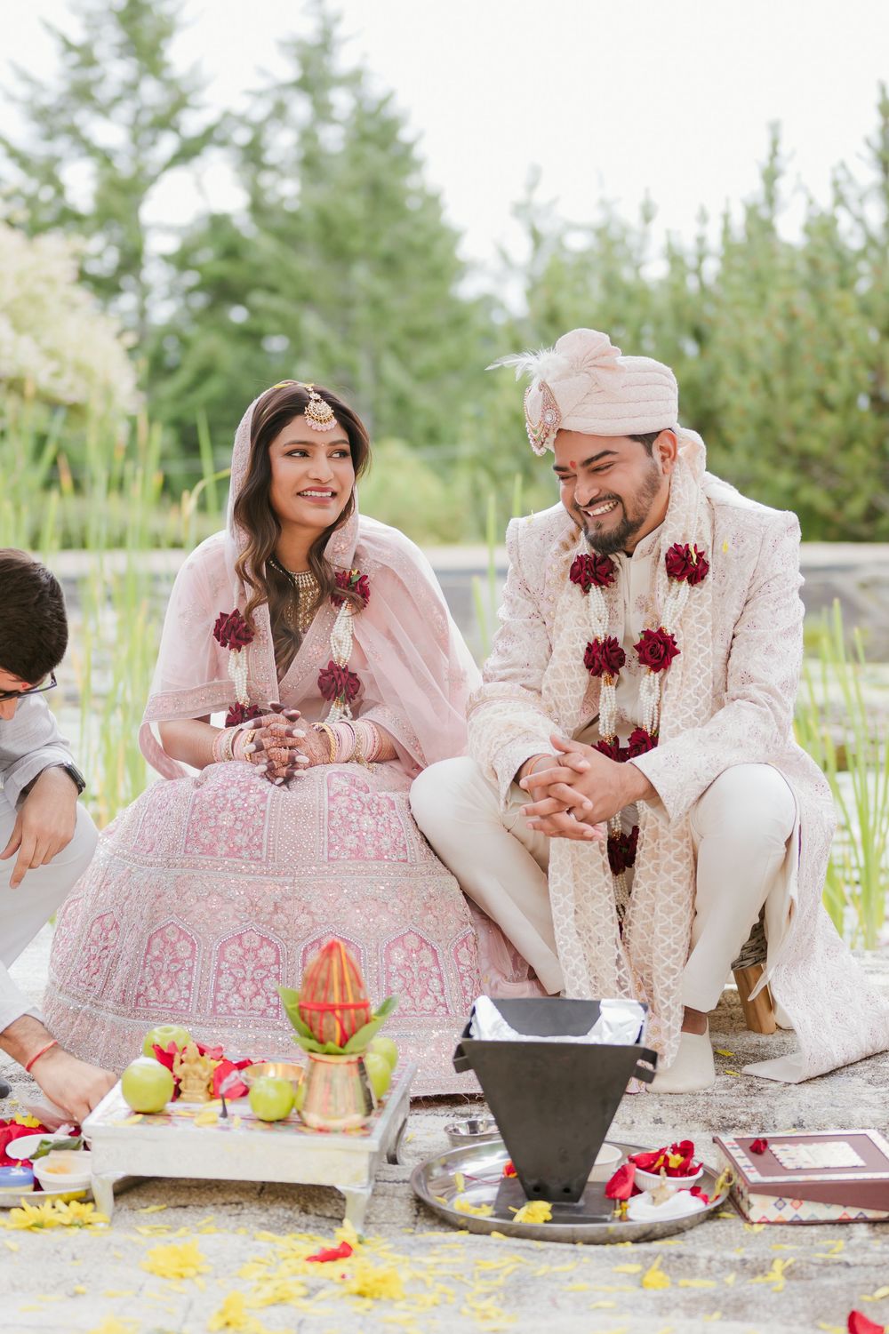 Traditional Indian wedding couple sitting on blanket with colorful decorations and snacks.