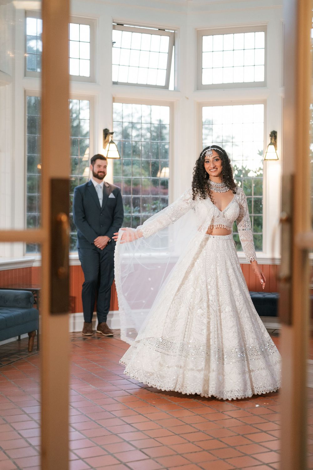 Bride in lace ballgown twirling in sunlit room with terra cotta floors.