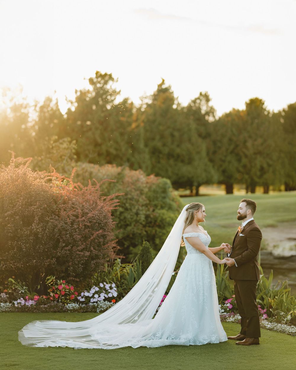 Wedding couple in formal attire posing in garden during golden hour.