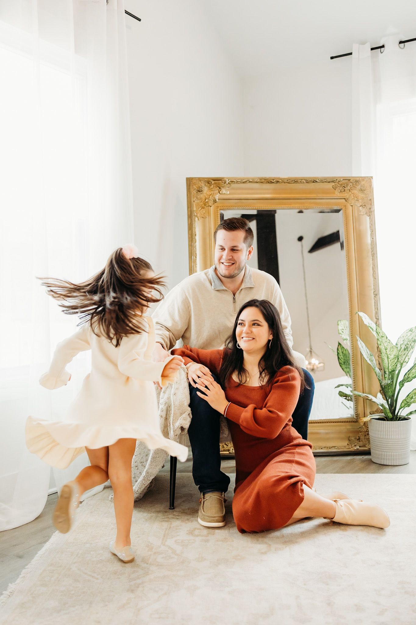 mom and dad sitting in a studio watching their daughter twirl around like a ballerina
