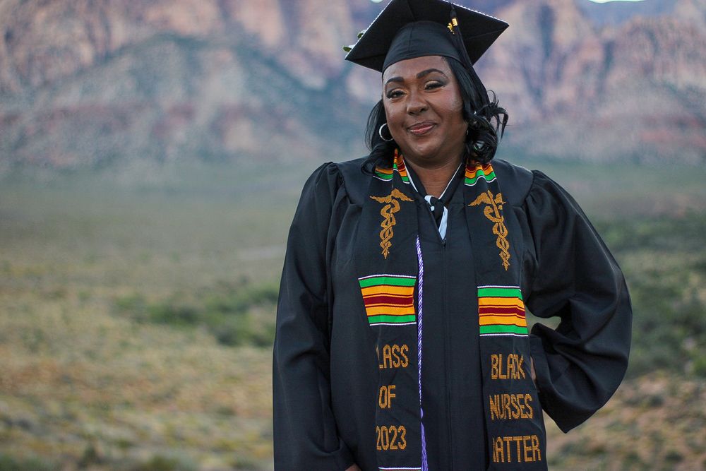 Black woman in graduation cap gown with Kente stole reading Class of 2023 Black Nurses Matter poses outdoors.