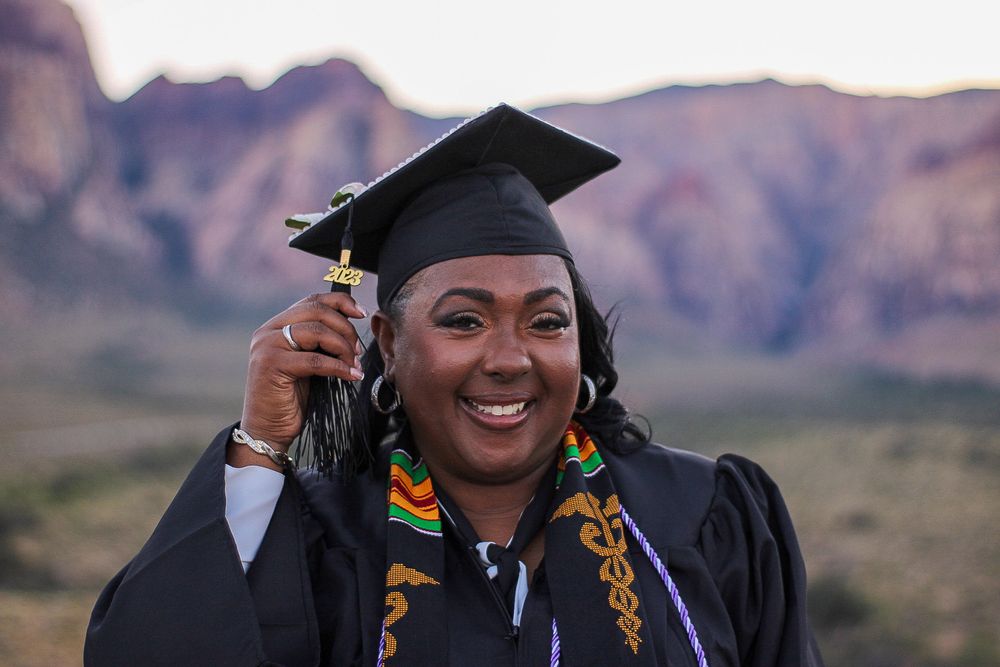 Joyful nursing graduate holding cap tassel in graduation gown at Red Rock Canyon Nevada.