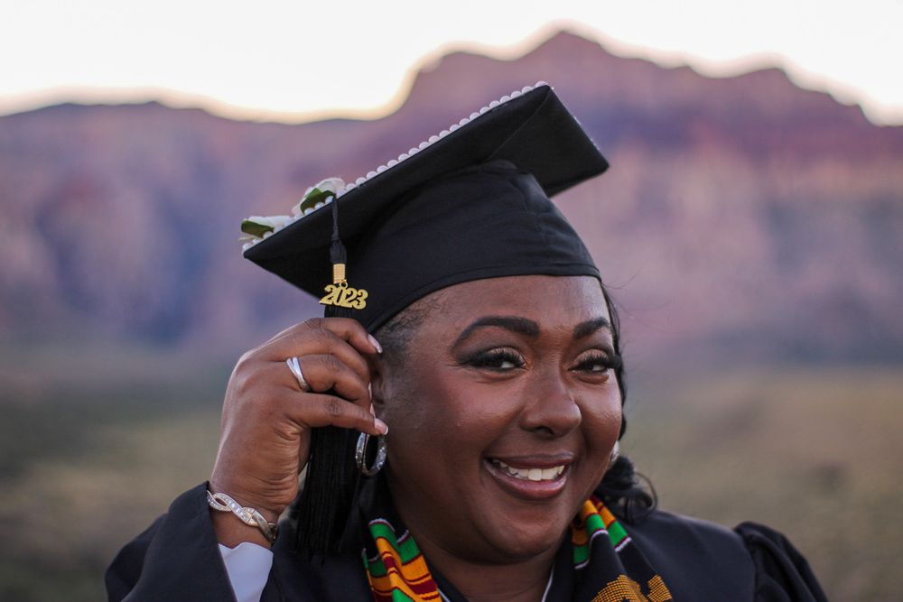 Laughing nursing graduate adjusting graduation cap with kente stole at Red Rock Canyon.